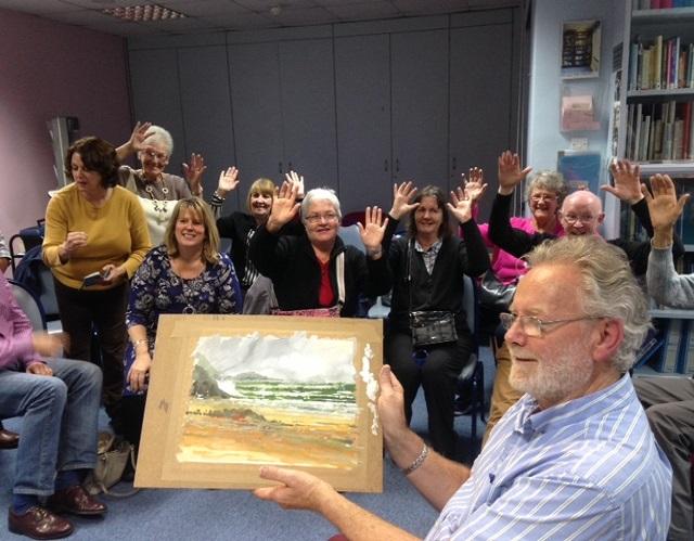 Artist holding up painting with happy members sitting behind
